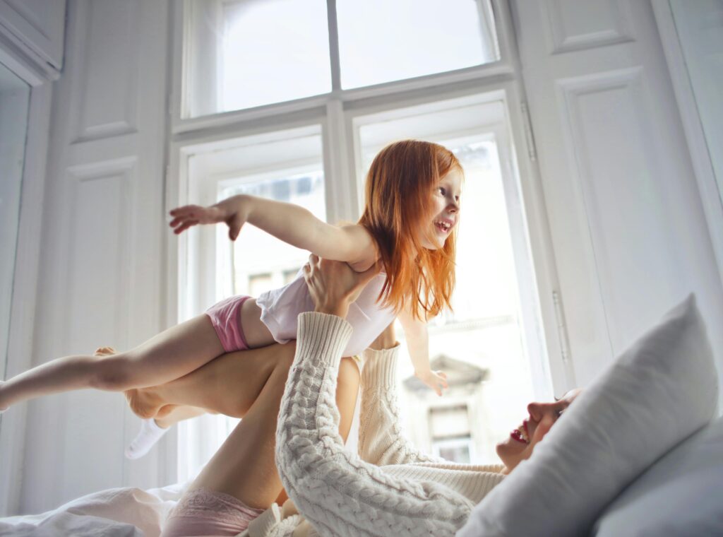 pexels-photo-3761510-3761510 Joyful mother and daughter playing together in a sunlit bedroom, enjoying a morning full of smiles and love.