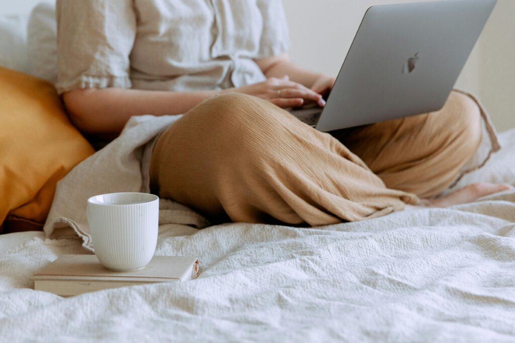 pexels-photo-3975583-3975583 Woman enjoying downtime, using laptop on bed with a coffee cup nearby, in a relaxed home setting.
