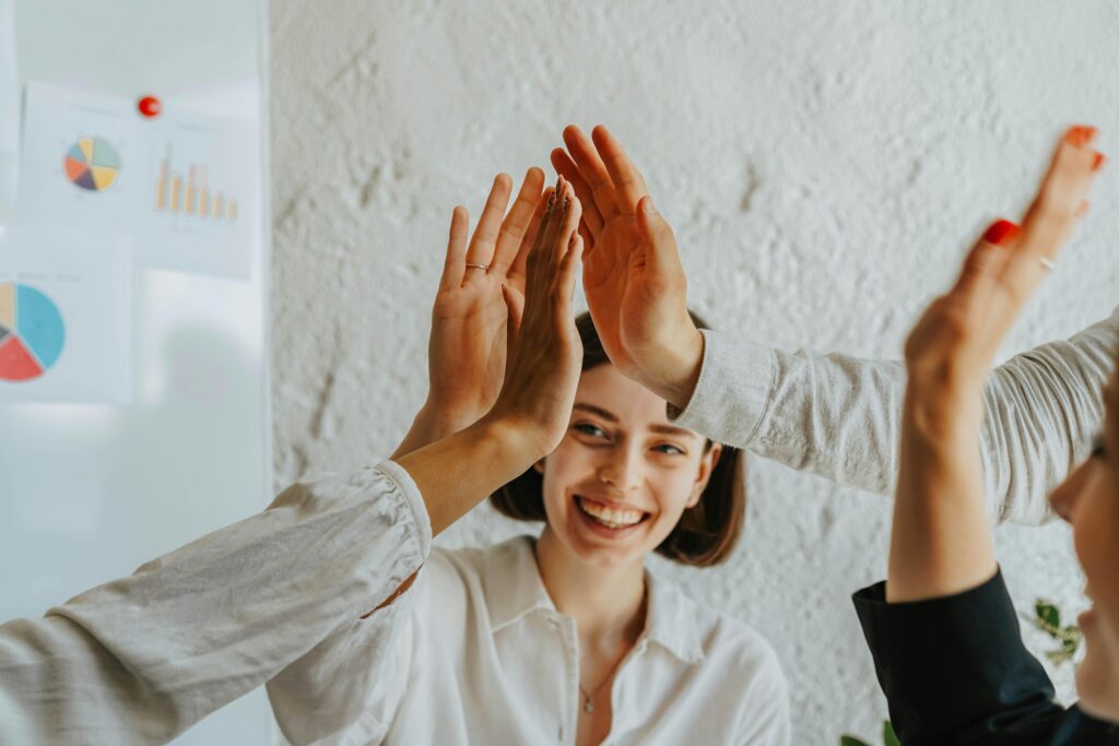 pexels-photo-8145330-8145330 Group of smiling adults engaging in a teamwork high five celebration in an office setting.